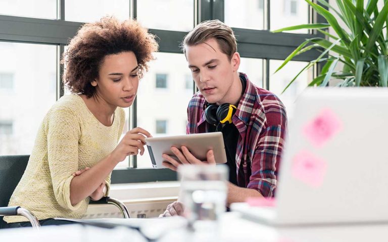 Two colleagues collaborating on a tablet in a modern office.