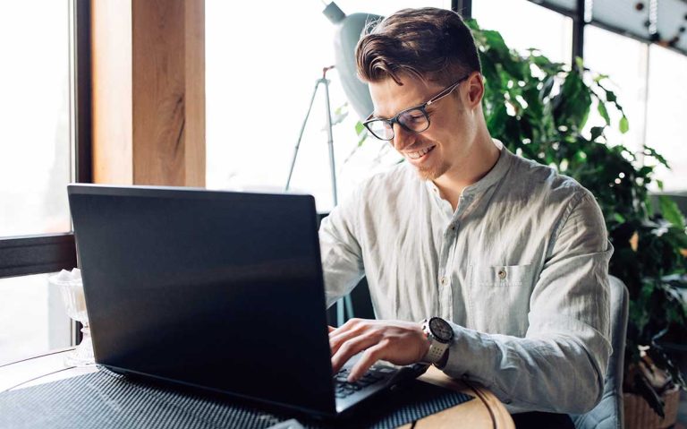 Man smiling and working on laptop in a bright room.