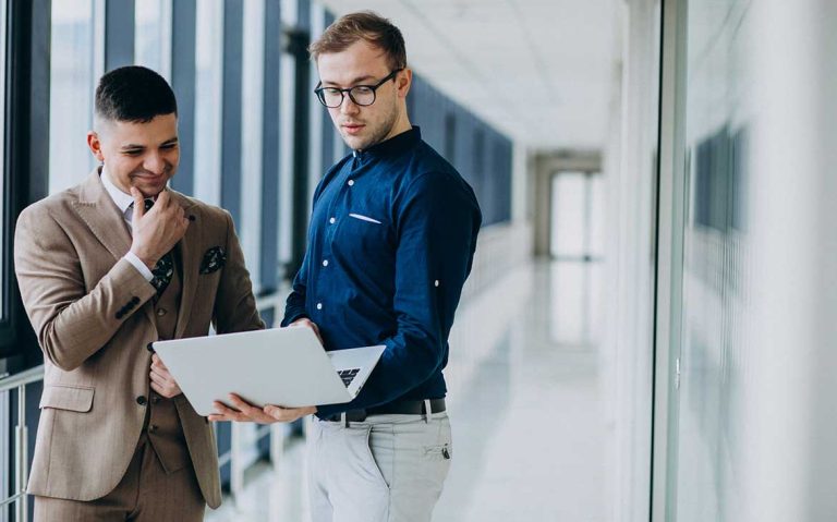 Two professionals discussing work while viewing a laptop in a modern office.