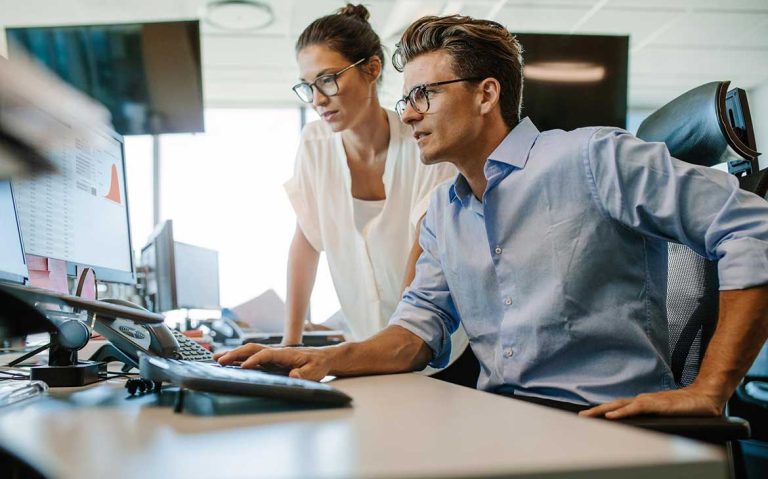 Two professionals collaborating in an office, focused on a computer screen.