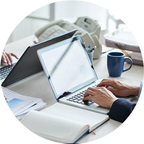 People working on laptops with notebooks and coffee on the desk.