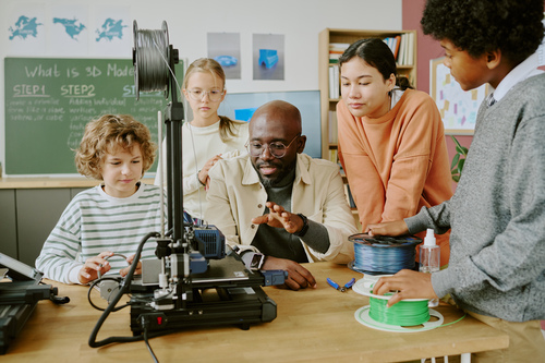 Teacher and students using a 3D printer in a classroom.