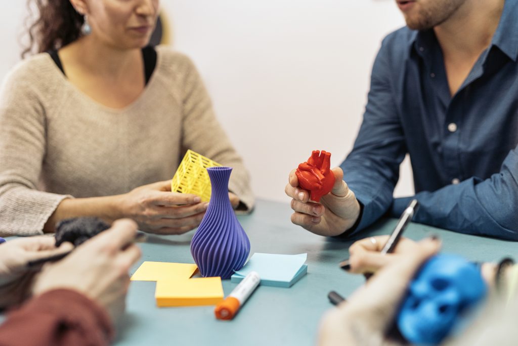 People collaborating with colorful 3D printed objects and notes.
