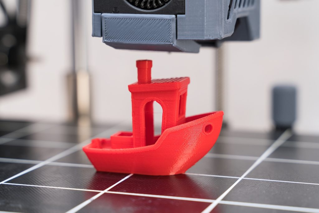 A red 3D-printed boat on a printer bed.